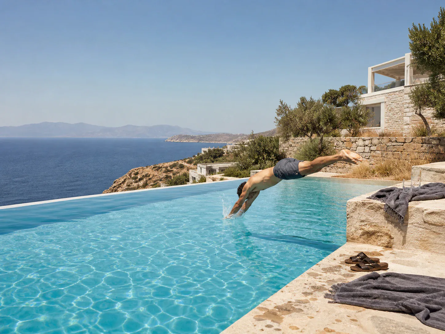 Editorial concept of a traveller diving into a private Aegean infinity pool