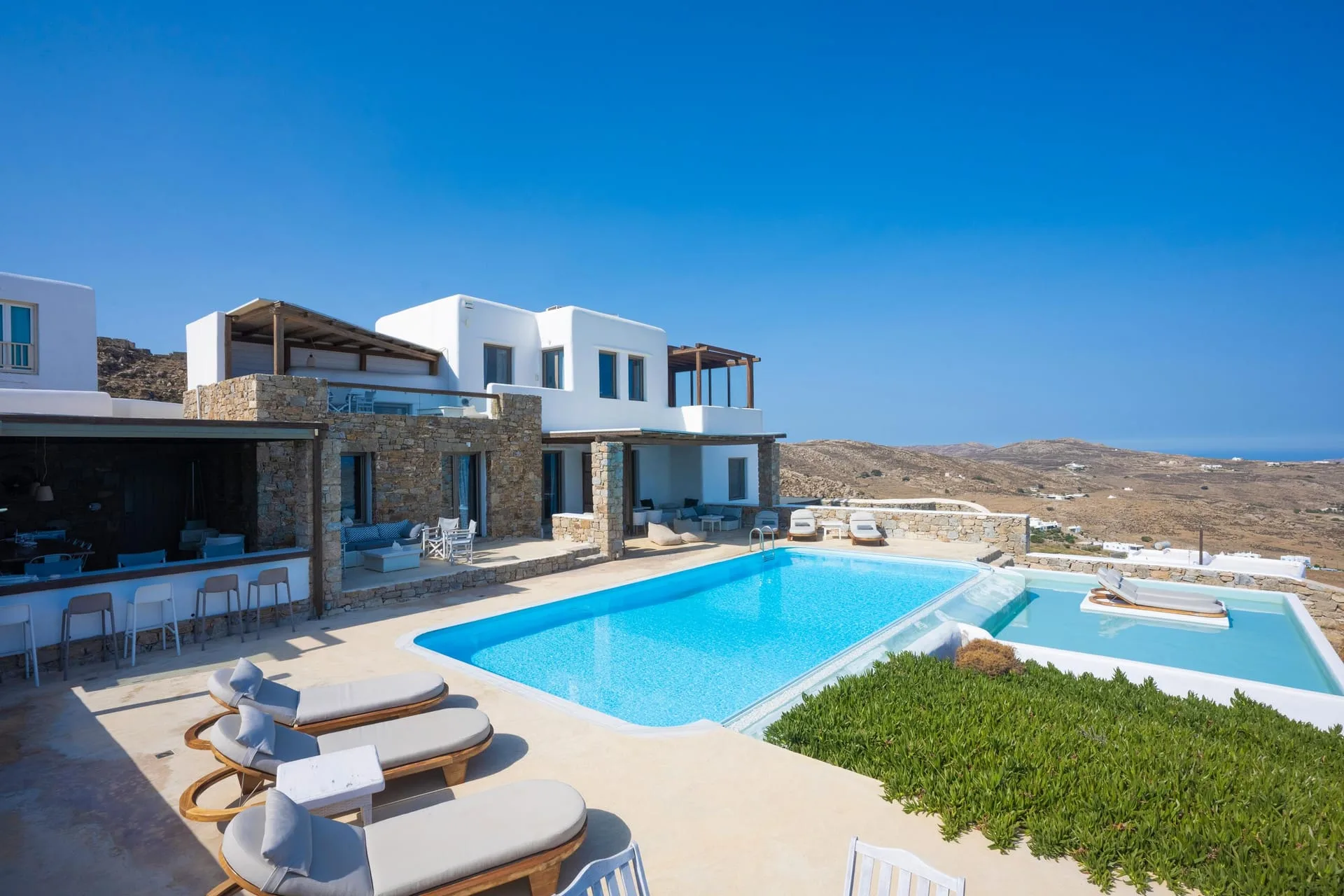A hillside villa whose terrace looks across dry hills to a strip of distant sea