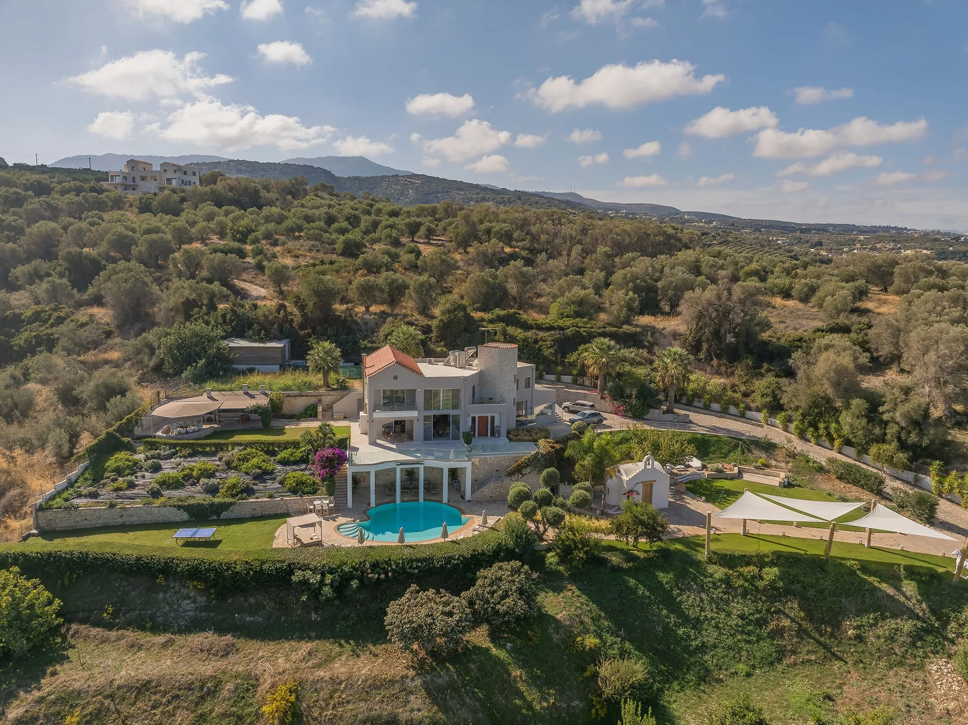 An estate villa in the Cretan hills at golden hour, with lawns, a pool and its own small chapel