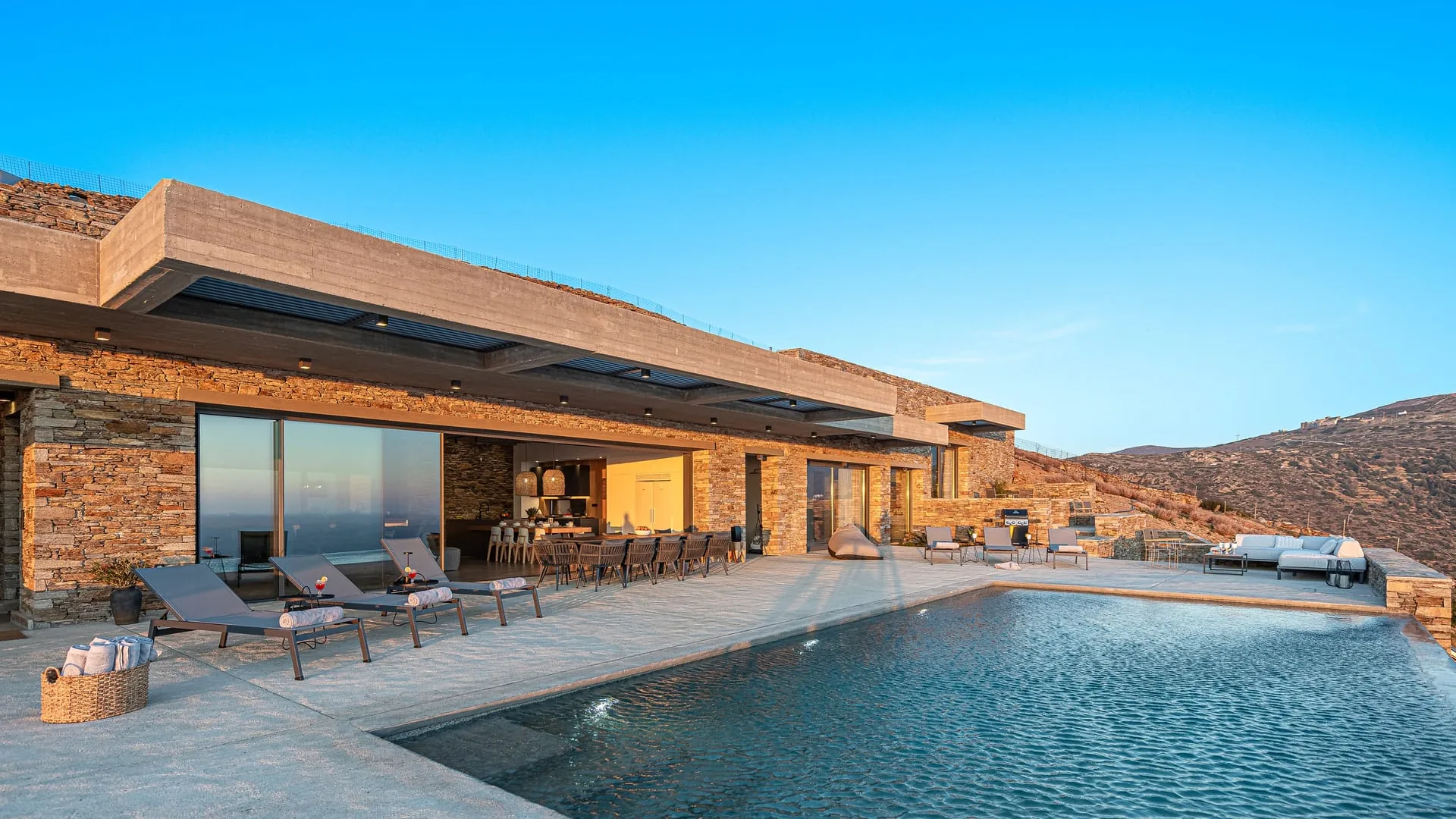 The stone terraces and pool of a Bnbstay villa in golden light on the hills of Andros