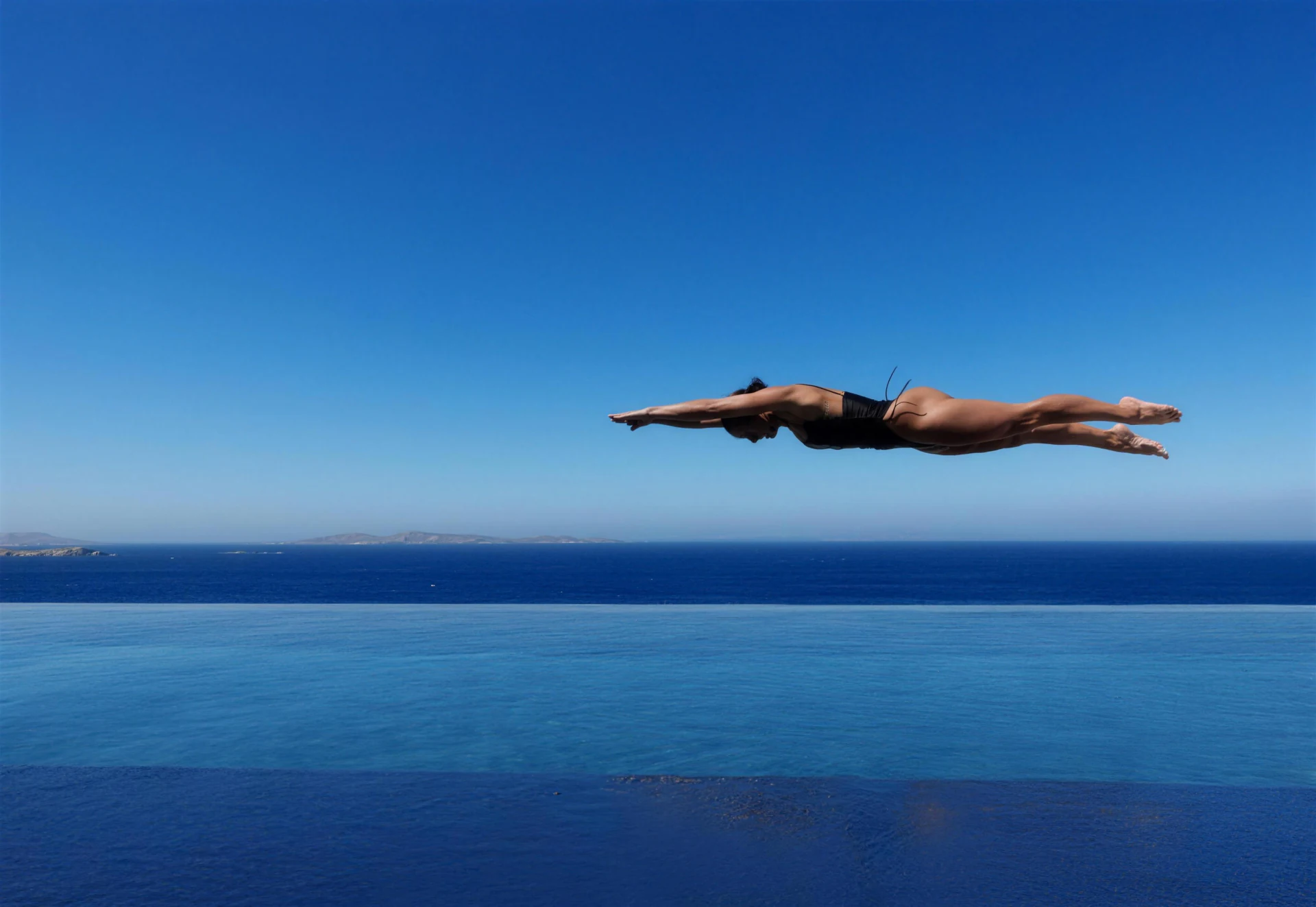 Editorial concept of a traveller diving into a private Aegean infinity pool