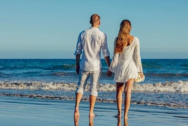 Couple in white walking hand in hand along the shore at sunset in Santorini