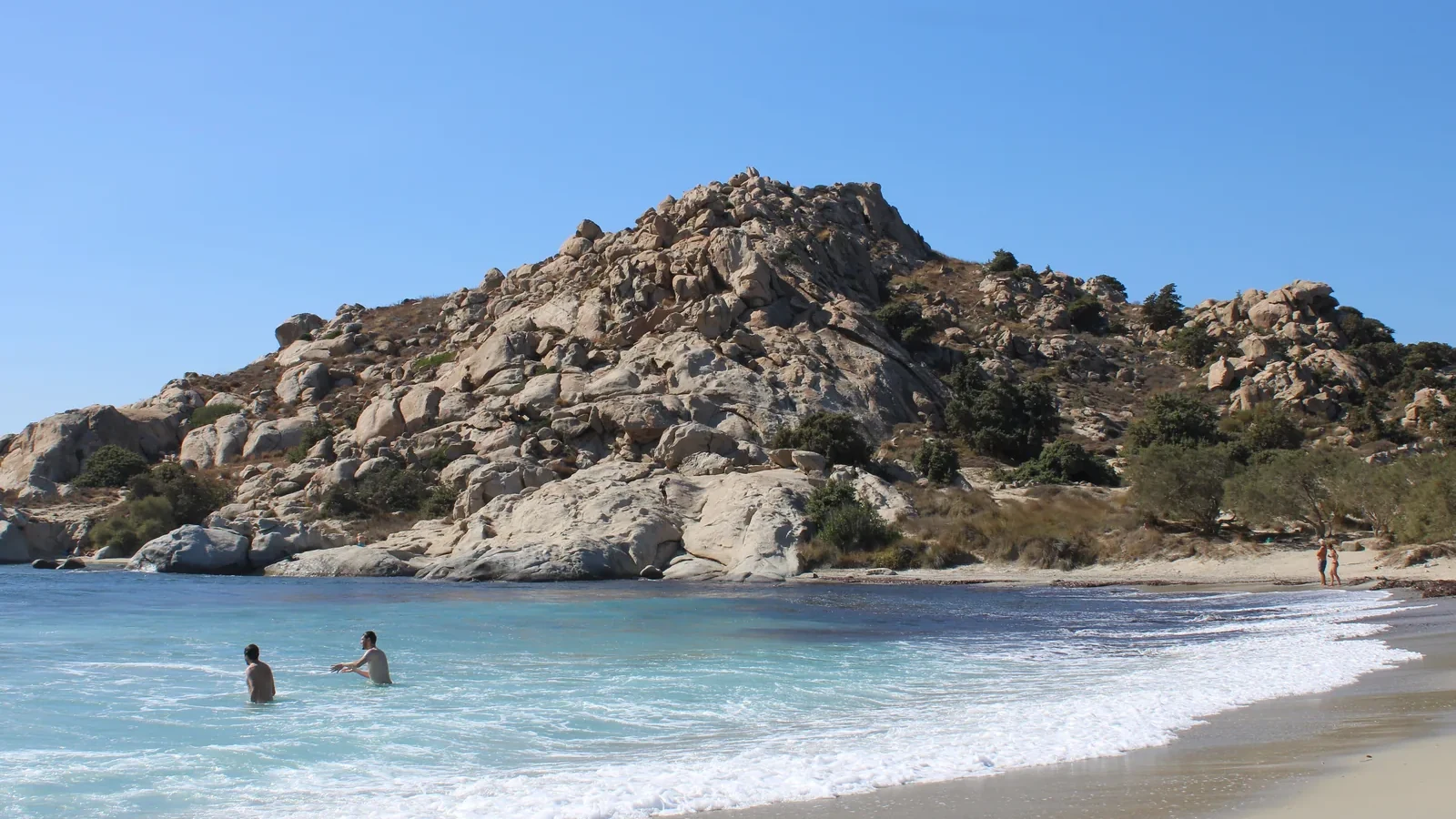 Swimmers in clear water beside the rocky headland at Mikri Vigla