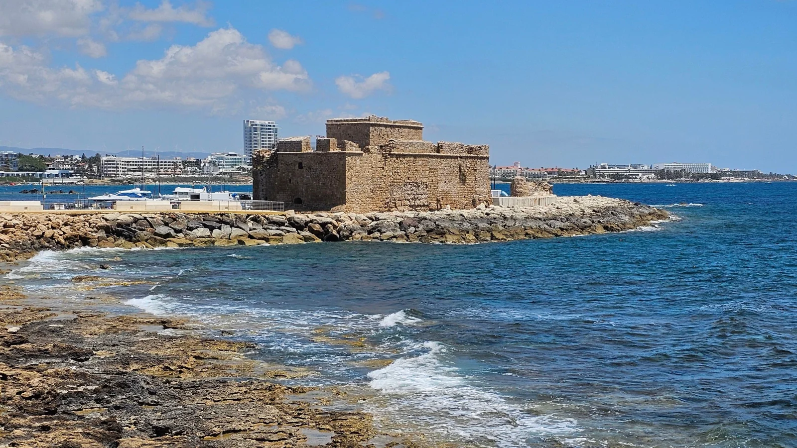 Paphos Castle beside the harbour, with rocks and waves in the foreground.