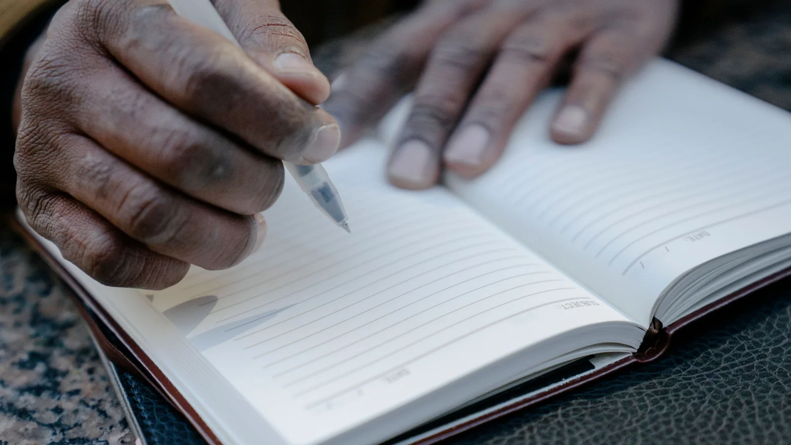 Hands holding a pen above an open lined notebook.