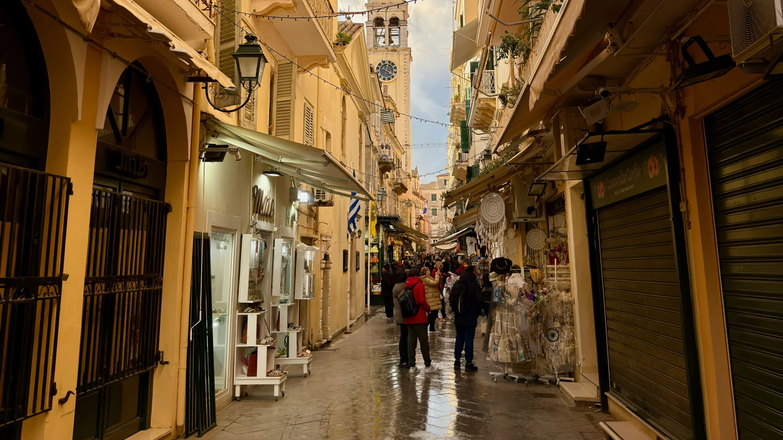 Pedestrians and small shops along a narrow street in Corfu Old Town.