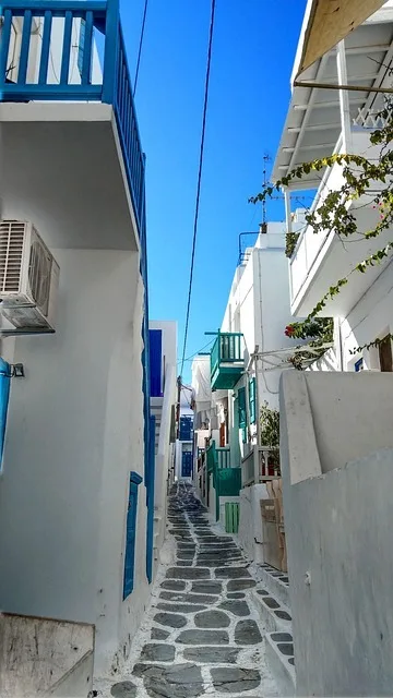 Narrow whitewashed Mykonos alley with a blue balcony and flowers