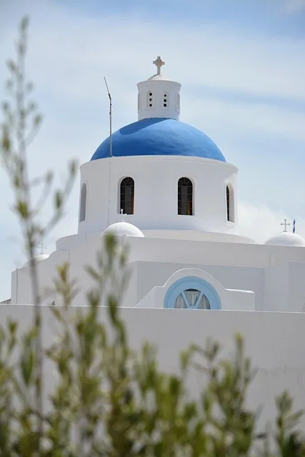 Whitewashed Santorini church dome and cross framed by olive branches