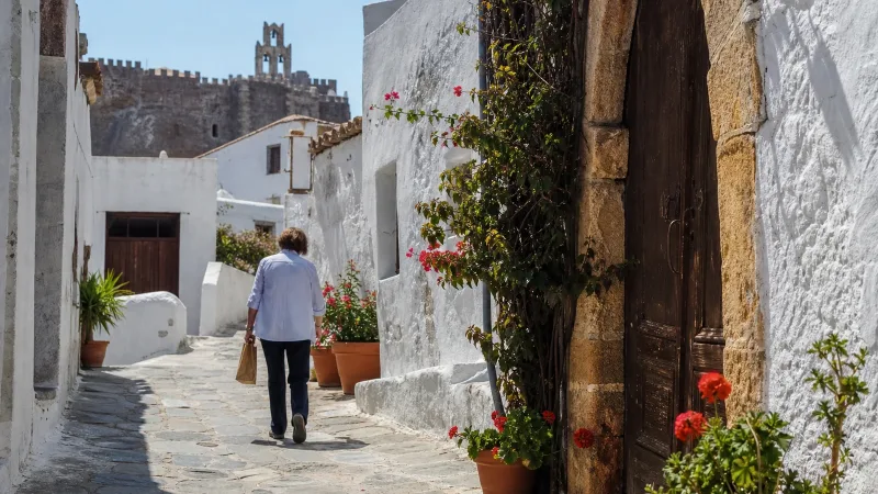 A local walking through a Chora lane on Patmos in late spring, with the Monastery of Saint John above