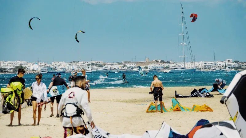 Kiteboarders rigging on the sand and riding whitecapped water during a summer meltemi on Paros