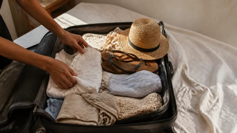 Traveller packing an open suitcase in a sunlit Greek villa bedroom