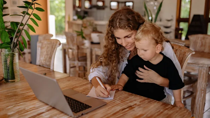 A parent and child making notes together beside a laptop.